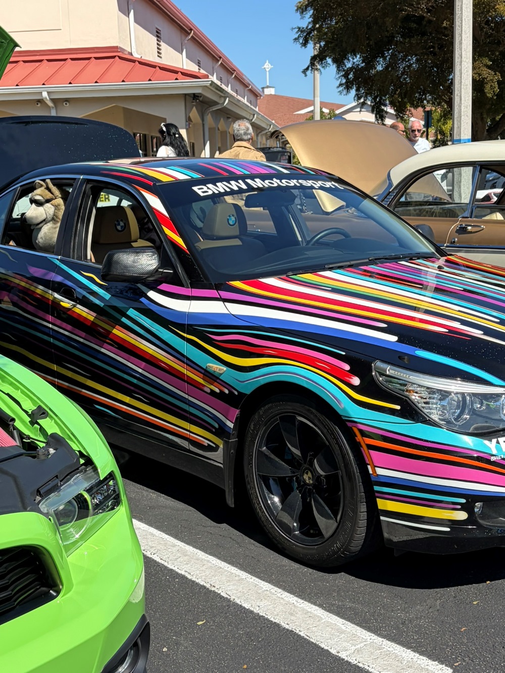 Black BMW sedan wrapped in colorful diagonal racing stripes parked between other cars